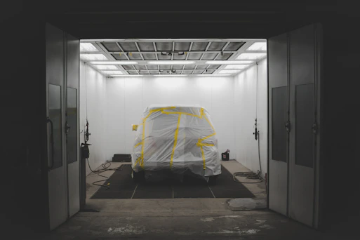 A technician carefully sanding and prepping a repaired area on a dark sedan with bright workshop lights overhead.