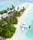 A secluded tropical island features a line of palm trees along a white sandy beach, with thatched roof structures integrated into the lush greenery. A seaplane is docked on the clear turquoise water near the shore, and a row of umbrellas with loungers extend along the beach.