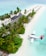 A secluded tropical island features a line of palm trees along a white sandy beach, with thatched roof structures integrated into the lush greenery. A seaplane is docked on the clear turquoise water near the shore, and a row of umbrellas with loungers extend along the beach.