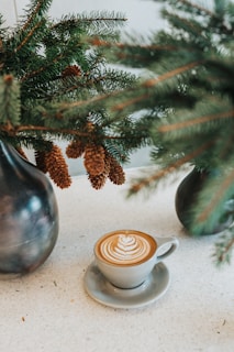 white ceramic coffee mug on saucer in front green leaves
