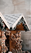 A festive market stall featuring a sloped roof adorned with green garlands and small red ornaments. The stall is decorated with an assortment of dried fruit and nut wreaths, shaped into stars and other designs.