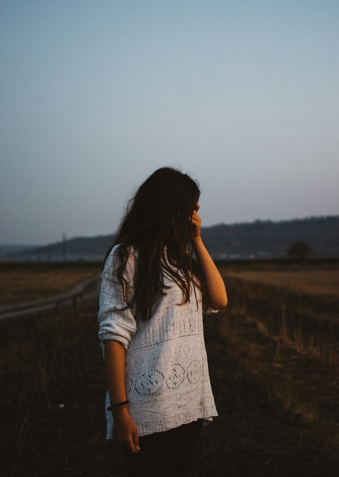 woman wearing white lace long-sleeved shirt covering her eyes beside road