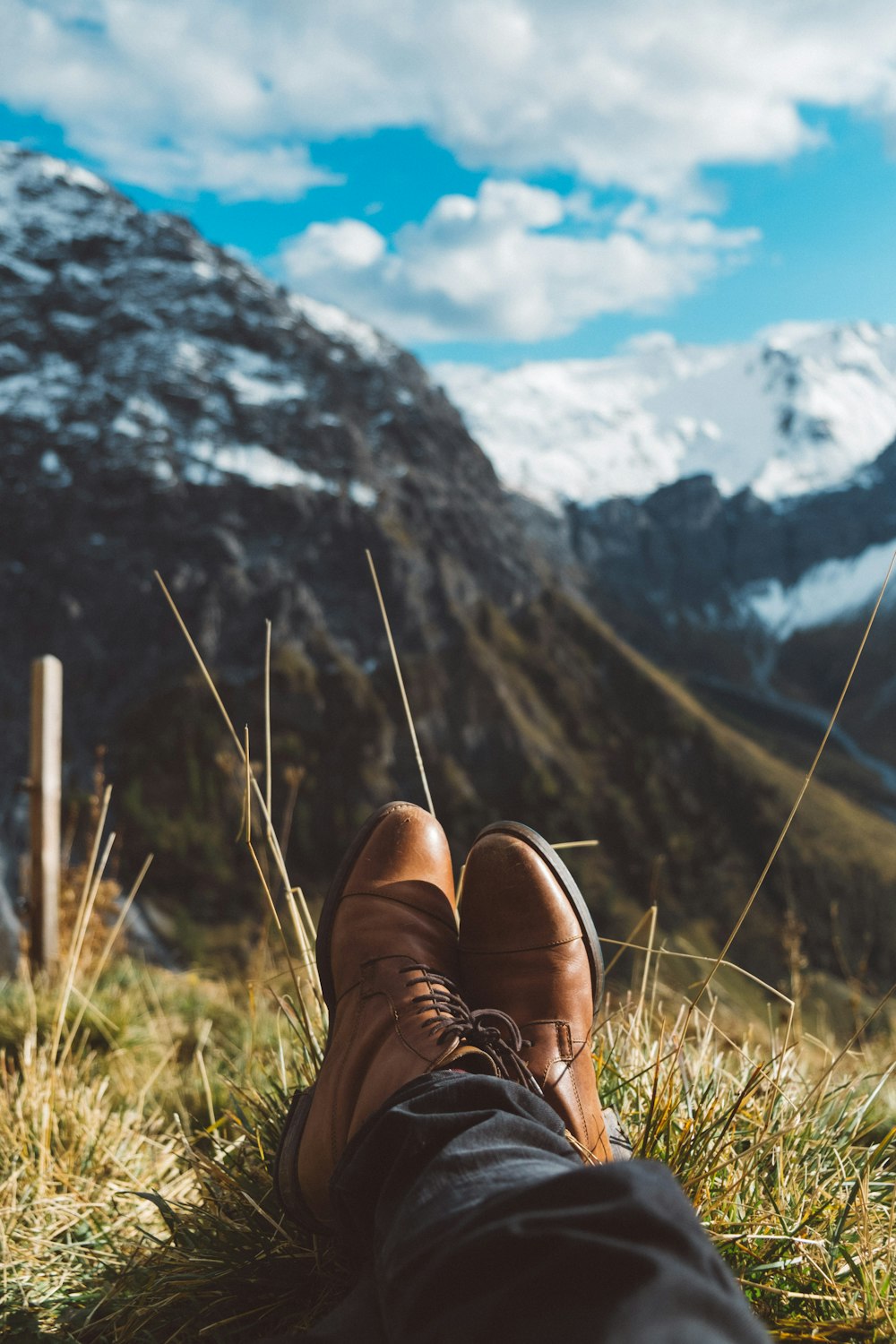 selective focus photo of person wearing brown dress shoes near mountains