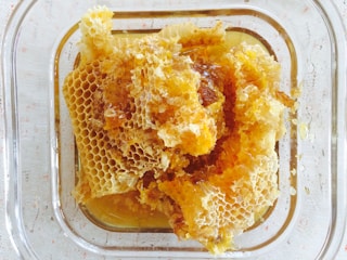 A close-up view of fresh honeycomb in a square glass container, with golden honey oozing from the hexagonal wax cells.