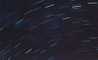 Long exposure photograph of the night sky capturing star trails in an arc pattern. These trails create a dynamic sense of movement against a dark backdrop.