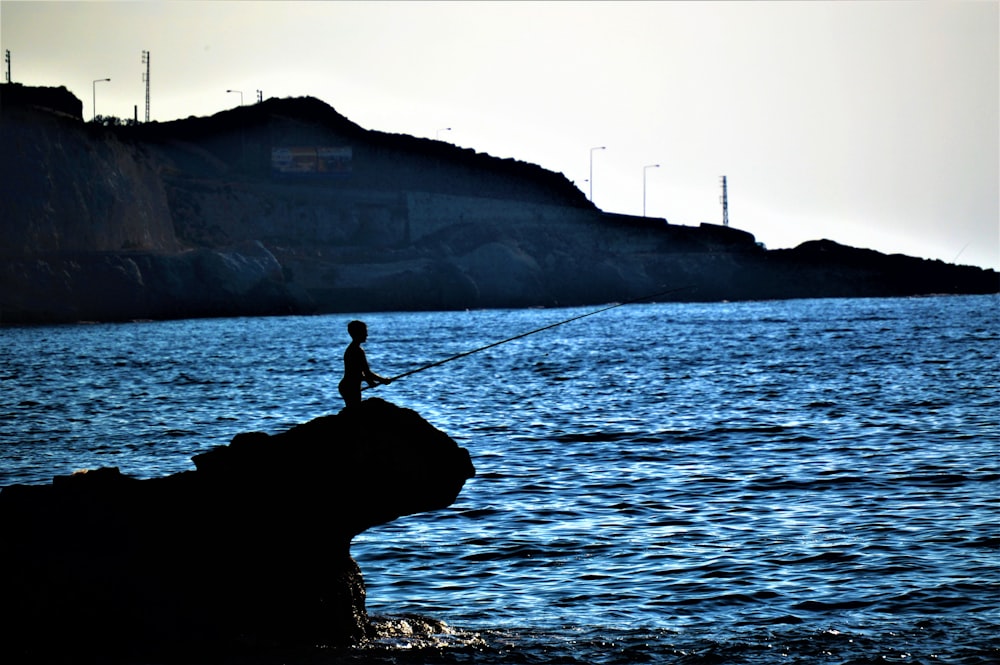 silhouette person fishing while standing on rock formation