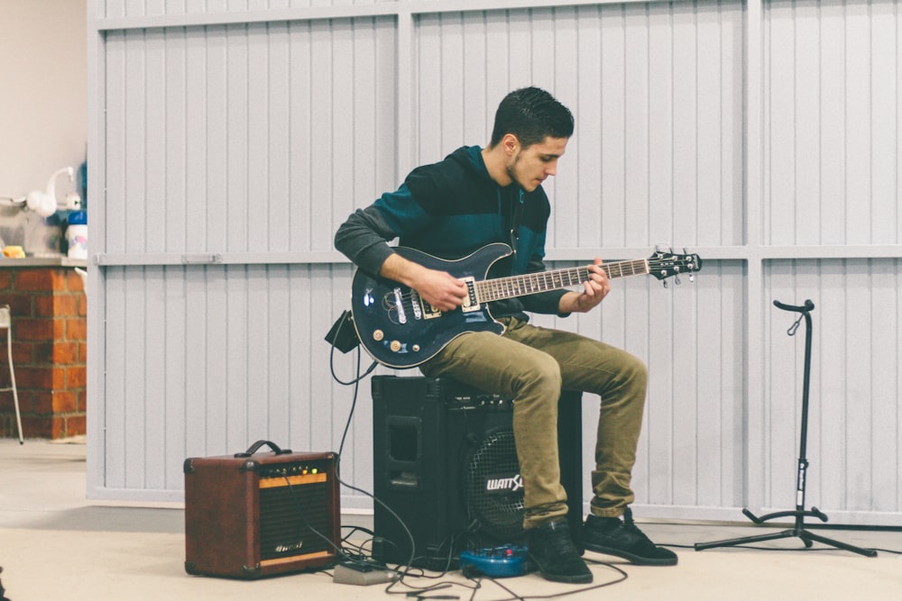 man sitting in guitar amplifier while playing guitar at daytime