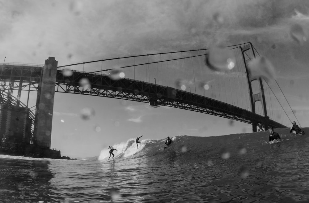 grayscale people surfing under bridge