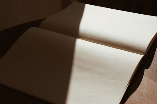 Detail of soft shadows falling on a simple wooden desk with an open notebook.