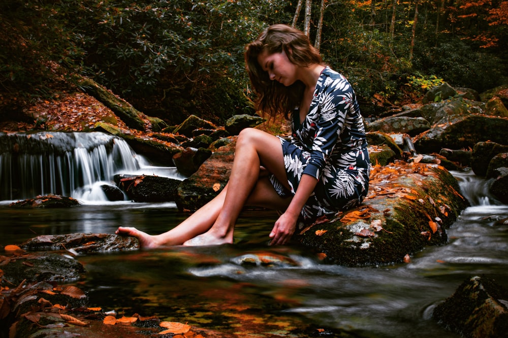 woman sitting on rock near body of water