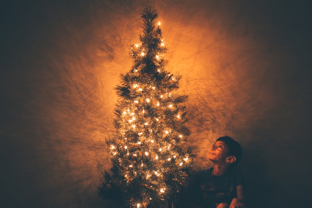 smiling boy beside Christmas tree with lighted string lights