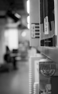 A black and white image of a library or bookstore shelf with books aligned vertically. A particular focus is on the spine of a book displaying musical content, as seen from the partial keyboard and 'Violin Play-Along' labels. The background is blurred, suggesting depth and giving focus to the foreground books.