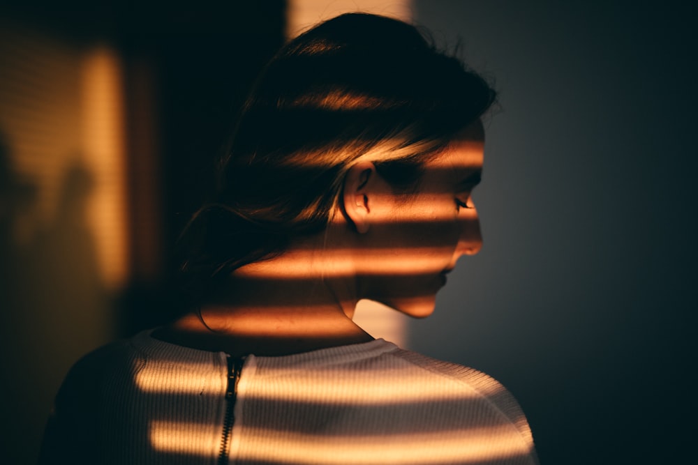 a woman standing in front of a window with the sun shining through the blinds