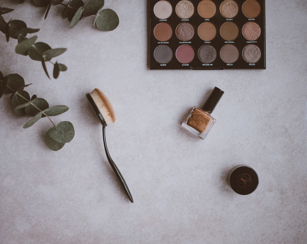 Neutral flat-lay of makeup palette, brush and eucalyptus