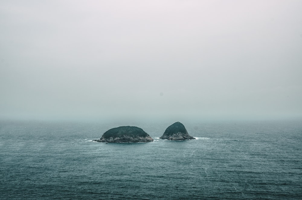 Duas formações rochosas cinzentas no meio do mar durante o dia