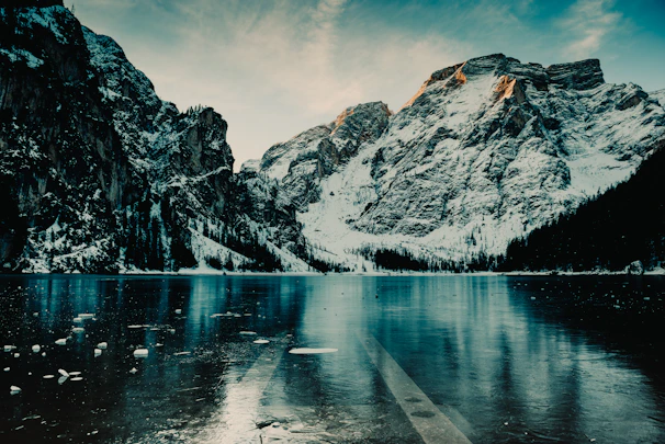 A serene frozen lake reflecting the icy peaks and a pale winter sky.