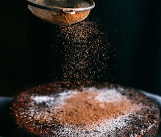 person pouring chocolate powder on cake