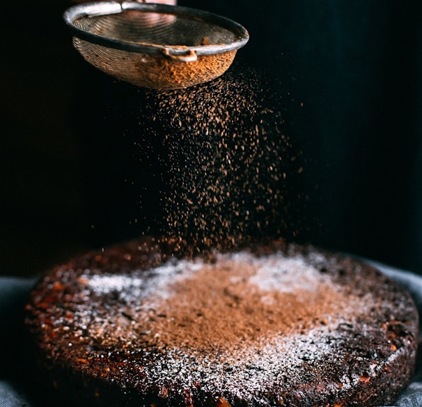 person pouring chocolate powder on cake