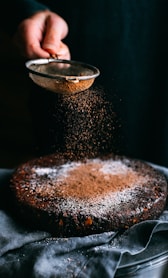 person pouring chocolate powder on cake