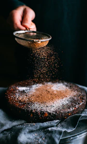 person pouring chocolate powder on cake