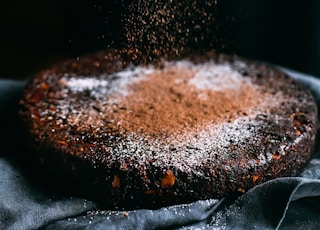 person pouring chocolate powder on cake