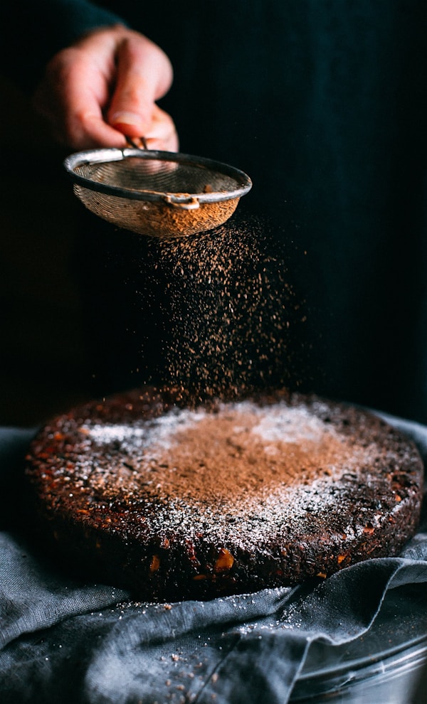Person pouring chocolate powder on cake