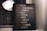 A motivational sign with various inspirational phrases such as 'LIVE FULLY', 'CREATE HAPPINESS', and 'LOVE DEEPLY' is placed next to a window with raindrops visible on the glass. The setting is dimly lit, creating a cozy and reflective atmosphere.