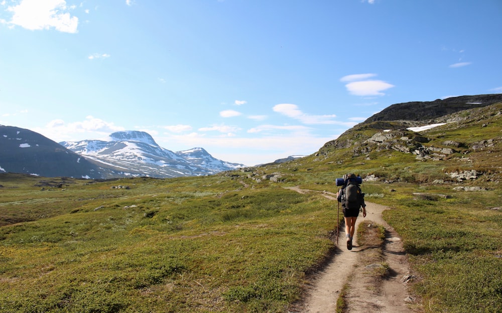 man walking between grass field mountain during daytime