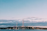An amusement park is situated by the waterfront, with various rides and tall structures visible. The sky is mostly clear with some scattered clouds, and several boats can be seen on the water. Buildings line the shoreline, adding to the scenic landscape.