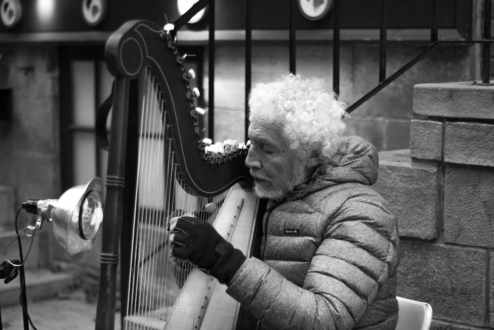 grayscale photo of man playing harp near stairs