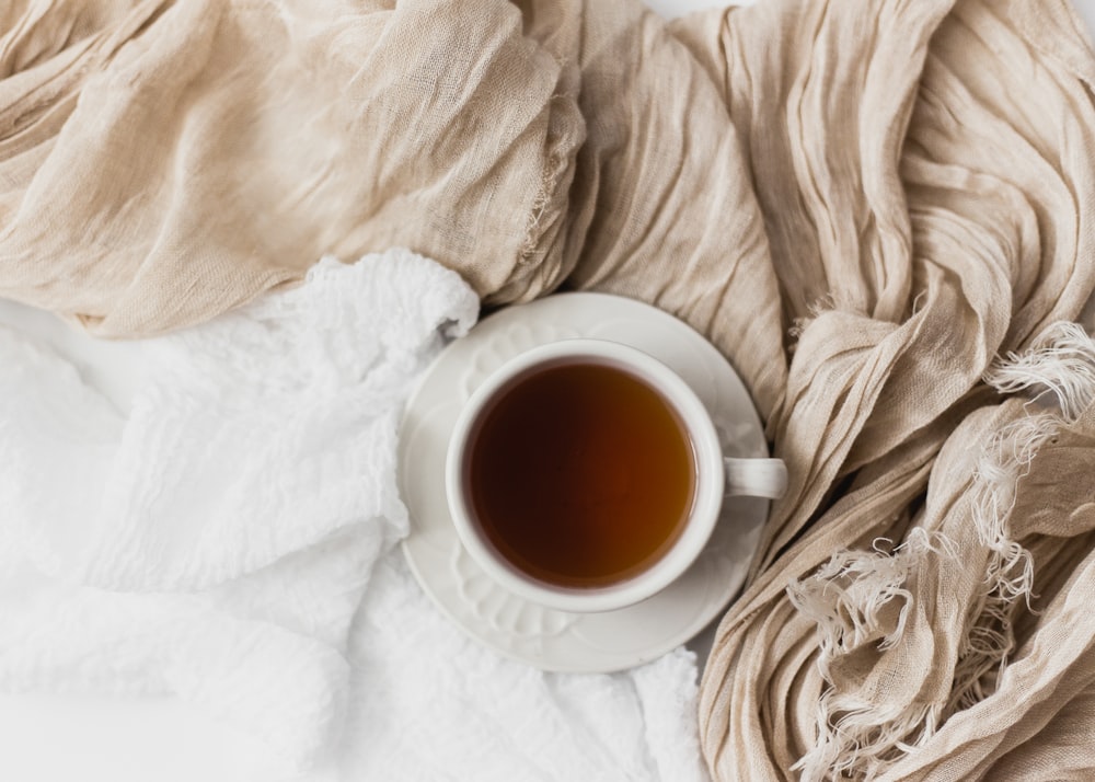 Tasse en céramique blanche remplie de thé sur soucoupe en céramique blanche