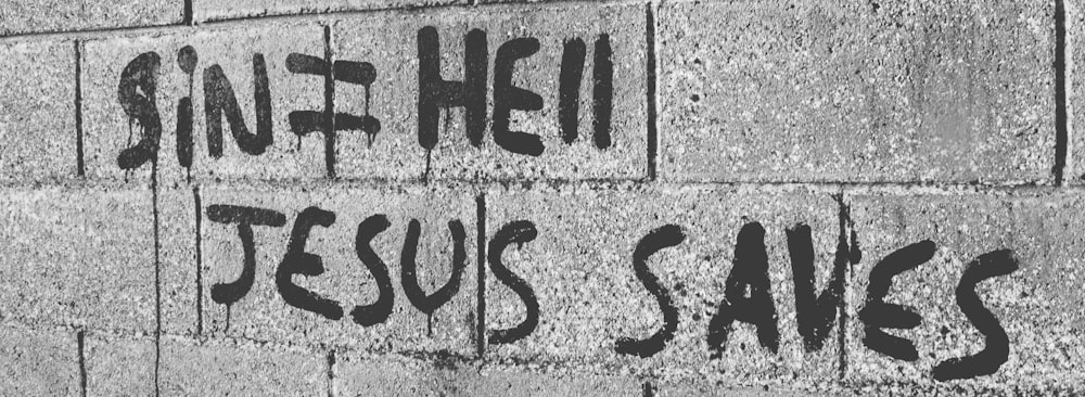 grayscale photo of hollow blocks wall with Jesus Saves text