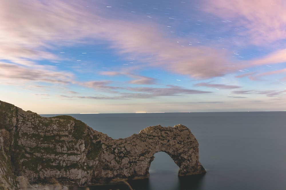 photo of arch cliff on body of water