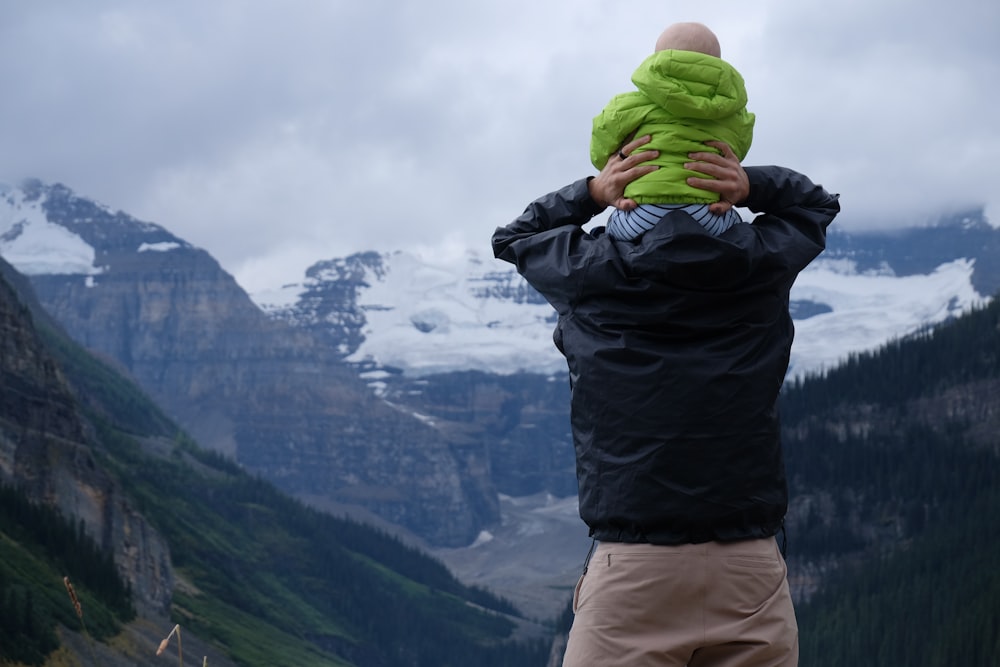 person carrying baby on his neck overlooking mountain