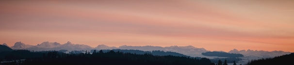 A panoramic view of a mountain range with hikers silhouetted against the sunset.