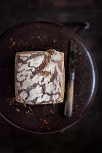 A rustic wooden table displaying freshly baked sourdough loaves wrapped in linen cloth with pomegranate accents.