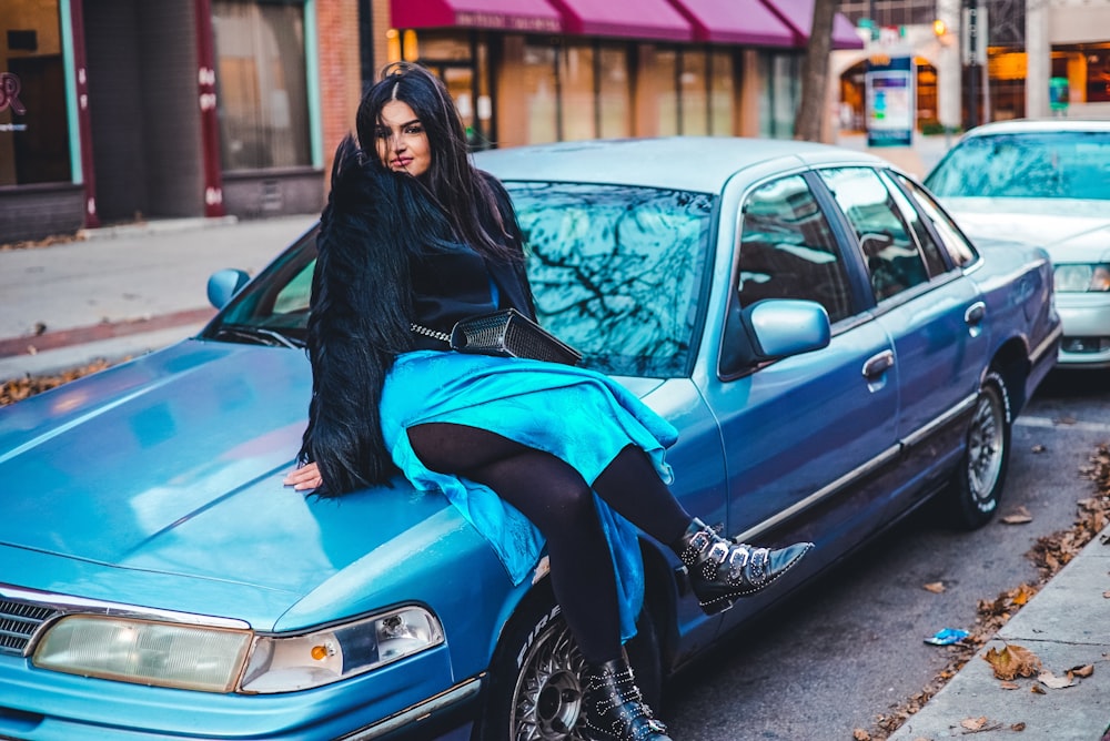 woman sitting on blue sedan on street