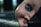 A close-up of a doll's face is partially broken and lying down. The blue eye is wide open, with details of its makeup clearly visible. Dirt and small scratches are present on the surface, adding a sense of wear or neglect.