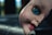 A close-up of a doll's face is partially broken and lying down. The blue eye is wide open, with details of its makeup clearly visible. Dirt and small scratches are present on the surface, adding a sense of wear or neglect.