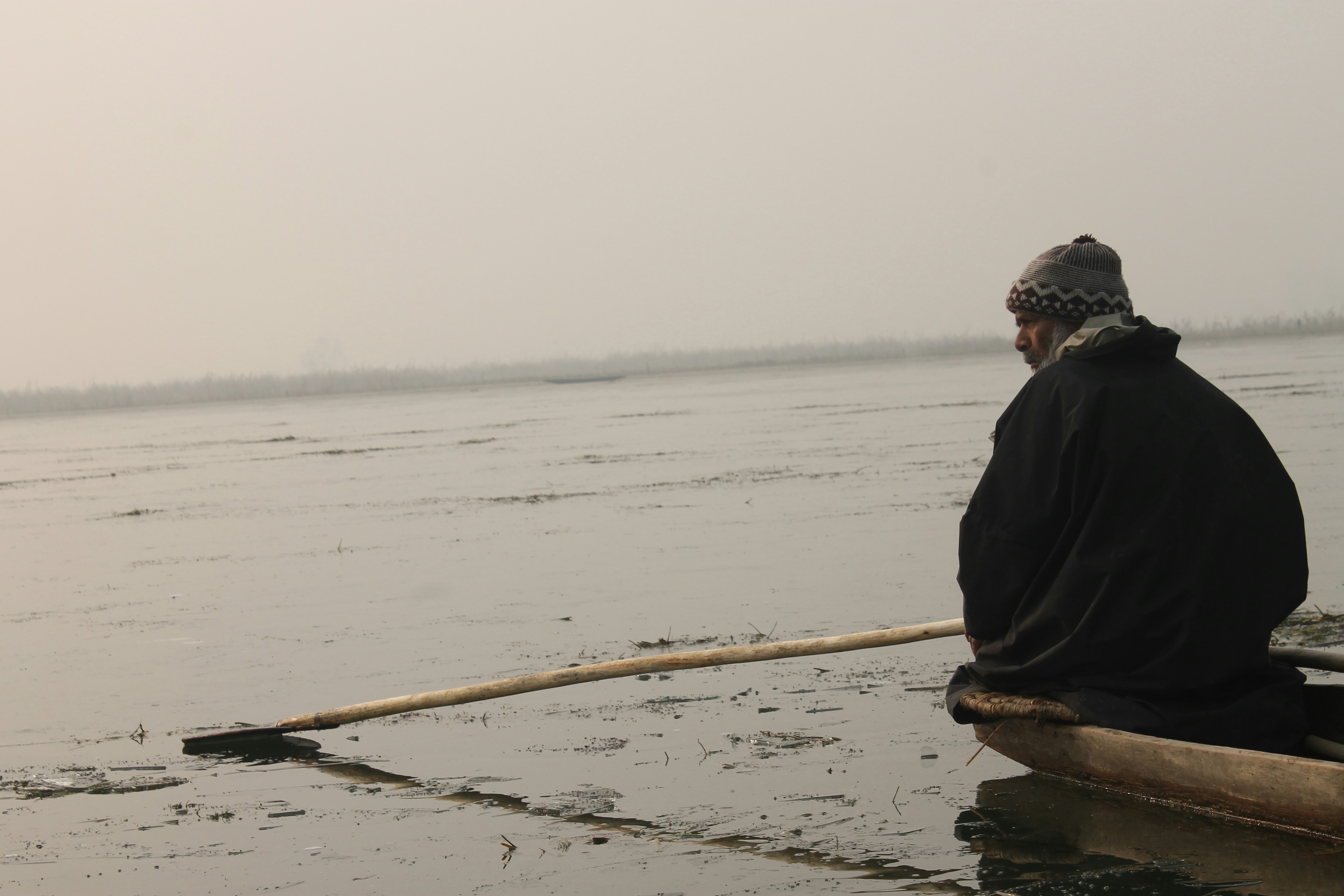 man looking sideways, I visited the Anchar Lake in Srinagar last year with my friend, on one winter morning to watch these poor fishermen work in extreme cold. These fishermen have to break the ice first and then look for fish, whose number is scant because of the high pollution levels in the lake waters.