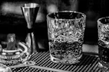 A moody, high-contrast shot of a vintage cocktail shaker resting on a dark wood bar surface.