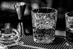 A moody, high-contrast shot of a vintage cocktail shaker resting on a dark wood bar surface.