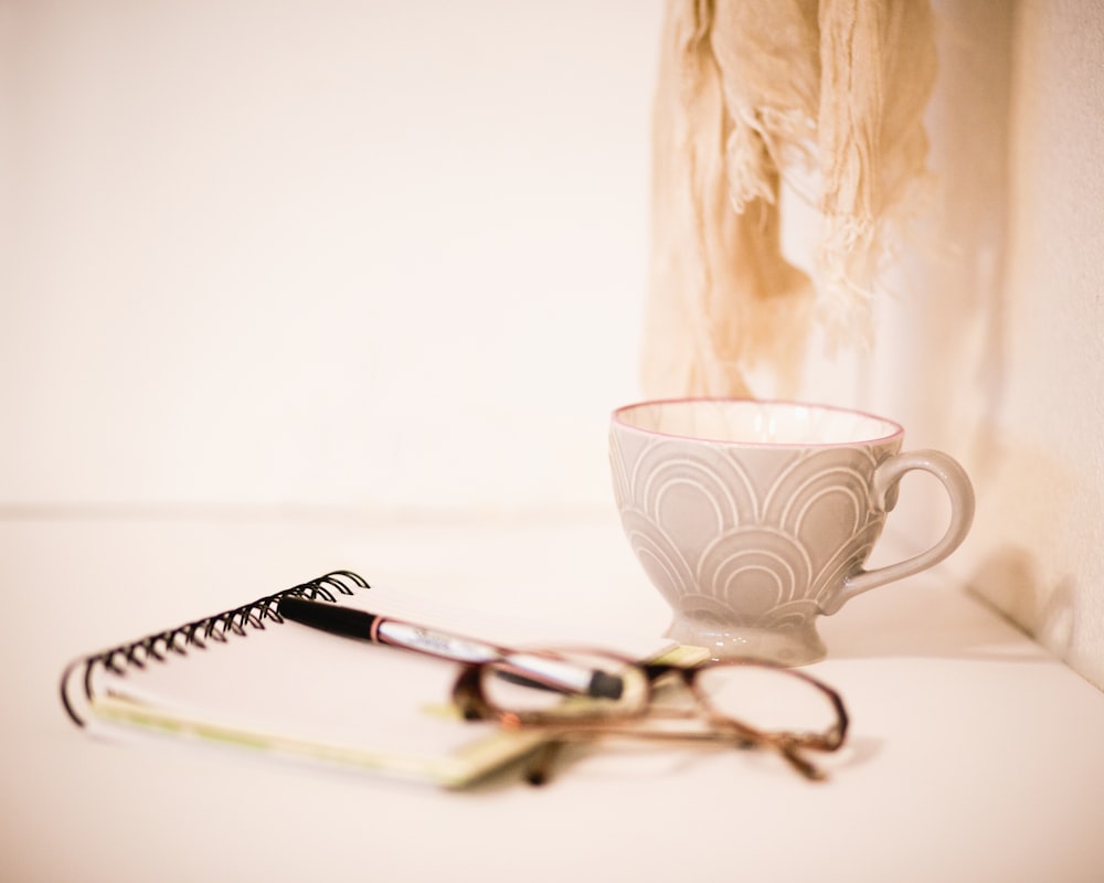 brown framed eyeglasses beside gray cup