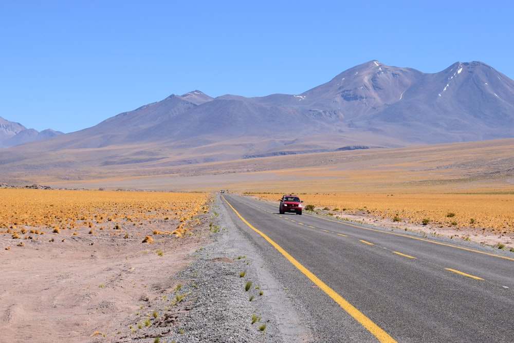 red vehicle on asphalt road toward mountains