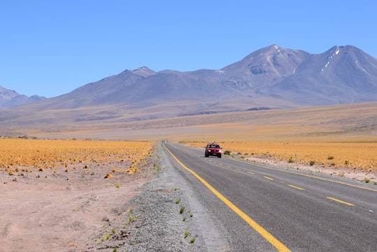 red vehicle on asphalt road toward mountains in Miscanti Lake Chile