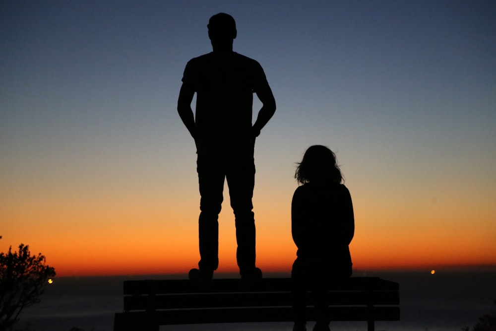 silhouette of an standing man and sitting woman on bench