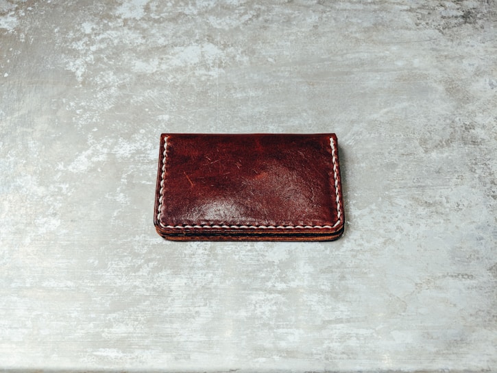 Close-up of a handcrafted natural leather wallet with detailed stitching on a dark wooden surface.