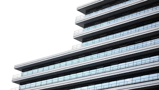 A modern, multi-story building is depicted, showcasing a series of horizontal lines and a sleek, minimalist design with extensive use of glass windows.