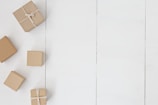Several small brown gift boxes with string tied around them are arranged on a white wooden surface. The boxes vary in size and are positioned on the left side of the image, leaving a significant portion of the white background visible.