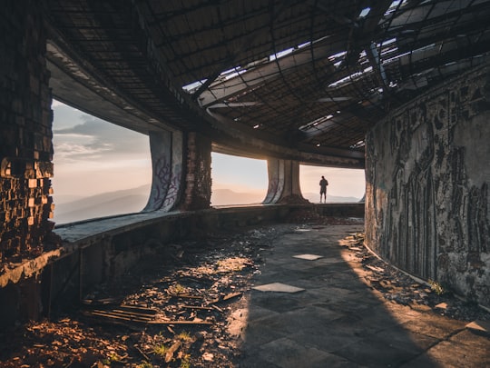 person standing on concrete beam facing mountain in Buzludzha Bulgaria